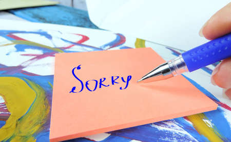 word sorry on pink notepaper, blue pen, Apologize