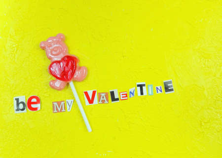 Be my Valentine - words made of paper cut letters and lollipop bear with heart on yellow backgroundの写真素材