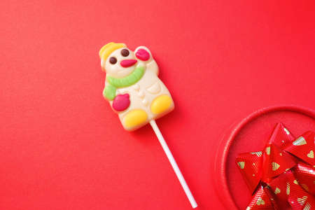 Snowman made of sugar candies. Merry Christmas and happy New Year greeting card. Lollipops of funny snowman Christmas present. Red backgroundの写真素材