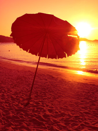 Blurred view of umbrella on sandy beach at summer sunrise sunset. Beautiful sunset beach. Romantic summer holiday and vacation concept for tourism.の写真素材
