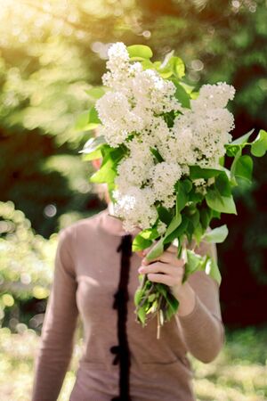 Beautiful young tender girl with a bouquet of flowers. Charming young lady with a bouquet of lilacs. photo without a faceの写真素材