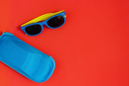 children's sunglasses with colored frames and a blue case for glasses in the shape of a car on a red...