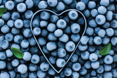 background of fresh frozen blueberries with a metal heart shape. Texture of blueberries close-up.の写真素材