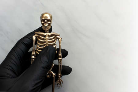 hand in a black glove holds the skeleton against a light background. concept of celebrating Halloween during quarantine.の写真素材