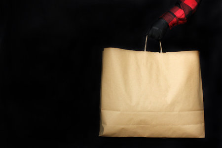 a man in black protective gloves holds a paper bag with purchases from the store during The black Friday holiday. The concept of selling and shopping in 2020 - the time of the coronavirus pandemicの写真素材