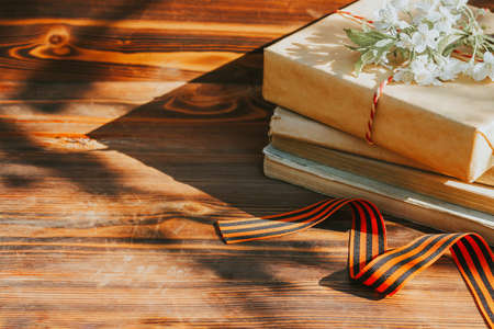 a St. George ribbon and a stack of old books on a wooden background with a sprig of a flowering tree. the concept of the Victory day on May 9 and historical notesの写真素材