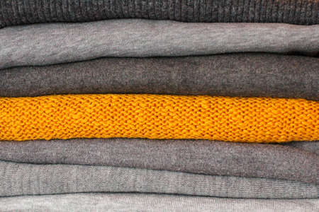 a stack of warm, cozy clothes for winter. among the gray sweaters, one is yellowの写真素材