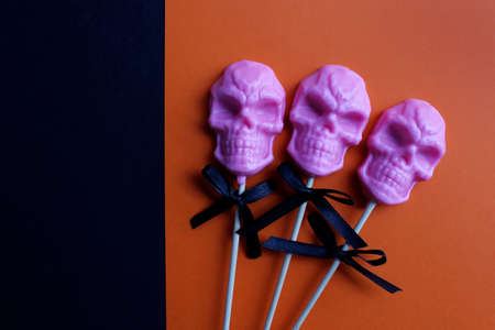three pink lollipops in the shape of a skull on a stick on an orange and black background. halloween concept.の写真素材
