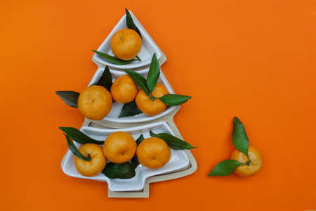 Tangerines in the shape of a Christmas tree on an orange background. Christmas food background, top...