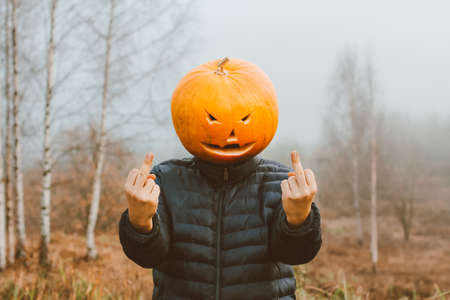 a man with a Halloween pumpkin on his head in a foggy field shows a fuckの写真素材