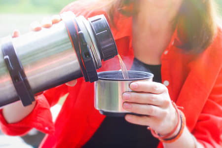 a girl pours tea from a on a walk. active recreation in the form of a walk through the forest and a stop for a picnic.の写真素材