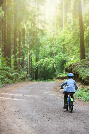 a small child in a helmet learns to ride a two-wheeled bicycle on forest paths. joint time of parents and children, active recreation.の写真素材
