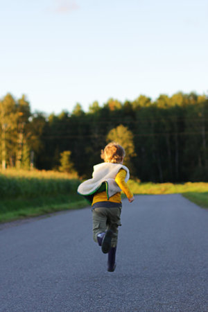 the child quickly runs away along the road into the distance. a fun childhoodの写真素材