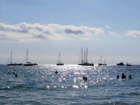 Bathers vacationing in front of sailboats at Es Trenc beach Mallorcaの写真素材