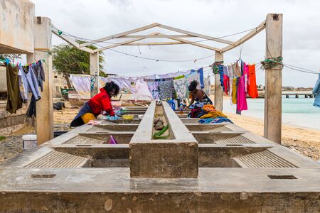 Sal Rei, Boa Vista, Cape Verde, Africa - February 8, 2018: Two women wash laundry by hand on a stone...