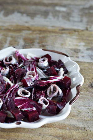 Marinated anchovies, radicchio lettuce and beets in a salad bowl in the shape of a shell on a wooden background の写真素材