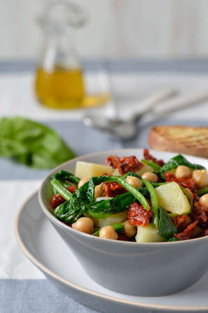 Salad light with spinach, chickpeas and potatoes with a salad bowl on the cloth surface with cutlery and bread toasts  bruschetta   Italian food の写真素材