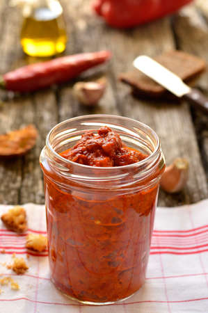 Ajvar in a glass jar on a wooden background, decoration  red pepper, olive oil, garlic, black bread の写真素材