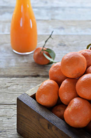 Whole tangerines  clementines  with green leaves in a wooden box  Freshly squeezed tangerine juice in a carafe  Close up の写真素材