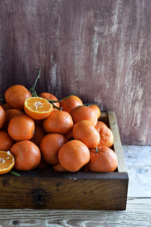 Group whole tangerines clementines  with leaves and tangerine, cut into halves in a wooden box on a...