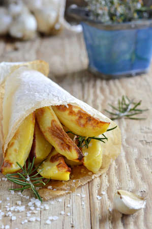 Roast potatoes with rosemary and garlic in cone of paper and decorations  branches of fresh rosemary and garlic  Close up の写真素材