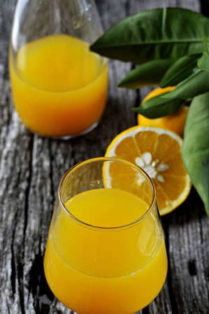 Freshly squeezed orange juice in drinking glass  Whole and halved oranges with green leaves  Close-up の写真素材