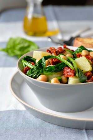 Salad light with spinach, chickpeas and potatoes with a salad bowl on the cloth surface with cutlery and bread toasts  bruschetta   Italian food の写真素材