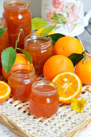 Several jars of orange marmalade homemade, fresh whole oranges with green leaves and oranges, cut in half の写真素材