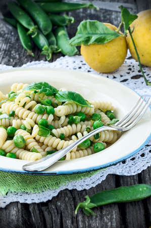 Italian Fusilli Pasta with holes with green peas basil and lemon zest on a wooden rustic table. Decoration pods of green peas lemon fruit.の写真素材
