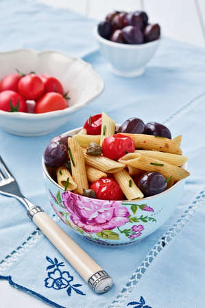 Penne pasta in a beautiful bowl with cherry tomatoes olives and capers. Italian cuisine selective focus.の写真素材