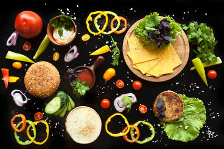 The composition of the ingredients for a burger on a black background. Appetizing picture about...
