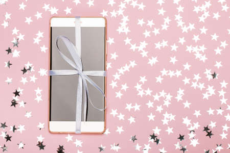 New phone, packed as a gift on a pink background, decorated with stars. The concept of the phone as a gift, the fulfillment of a dream. Flat layの写真素材