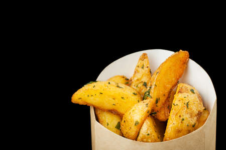 Slices of delicious fried potatoes with spices in a cardboard box on a black background. Place for textの写真素材