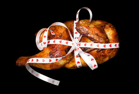 Luxury appetizing grilled chicken packed ribbon as a gift on the black background. Concept of surprise at the restaurant or cafe, shares in the social network, Valentine's Day joke, etc.の写真素材