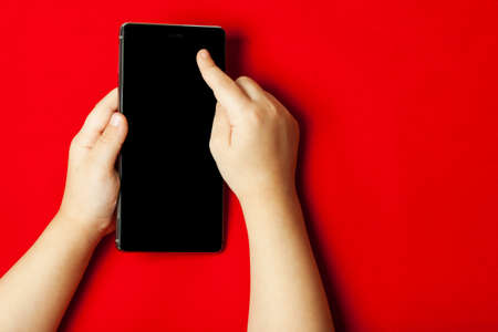 Smart phone in the hands of a child on the red backstage.  The concept of necessary things a little...