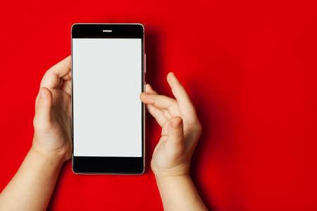 Smart phone in the hands of a child on the red backstage.  The concept of necessary things a little girl, technology for children. Flat flyの写真素材