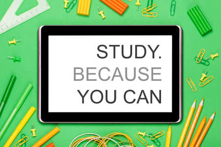 A tablet on a green background surrounded by school or office supplies. Yellow, orange and green colors. Study because you can. The concept of creativity, education, ideas, school, office, etc.の写真素材