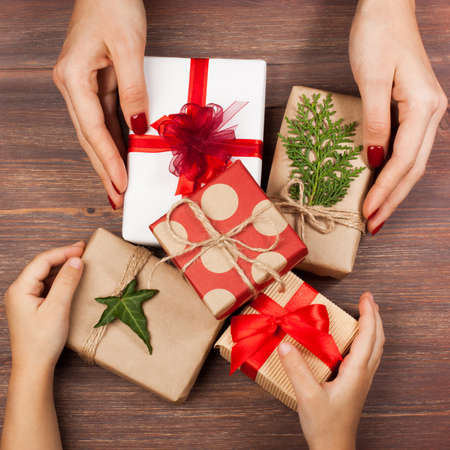 Handles of mother and child holds gifts packed in a minimalistic style on a wooden background. The concept of stylish, minimalistic holidays, hipsters, trends, New Year, Christmas, birthday, etc.の写真素材