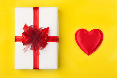 White box with a red ribbon on a bright yellow background with a heart. A nice gift for a loved one. The concept of Valentine's Day, Christmas, Birthday, etc.の写真素材