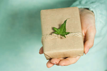 Beautiful female hands with packaged cute gift on a soft mint background. Concept of the New Year, Christmas, Valentine's Day, giftsの写真素材