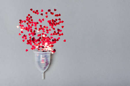 Transparent menstrual cup with red hearts on a grey background