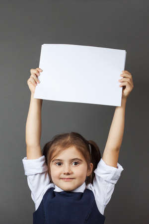 Little girl in a school uniform show an empty paper. Copy space. The concept of education, back to school, etc.の写真素材
