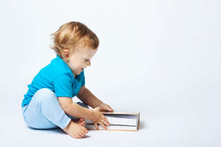 Cute baby boy playing with book on the white background. Copy place. The concept of teaching children to read, love of books, childrens literatureの写真素材