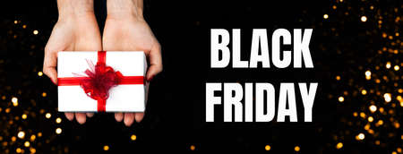 Banner for sale on Black Friday. Lovely female hands holding a bright gift with a red bow.