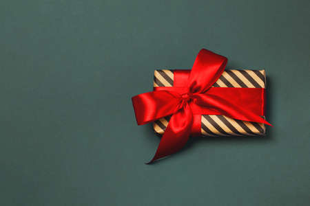 Luxuriously wrapped gift with red ribbon on the dark gray background. Trendy colors. Copy space. Merry Christmas, St. Valentines Day, Happy Birthday and other holidays concept.の写真素材