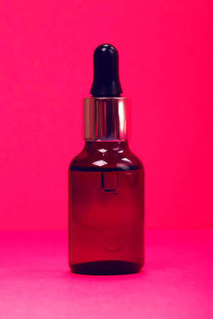 Face serum close-up on the trendy neon pink background. Collagen, hyaluronic acid for skin care. Achievements of modern science in cosmetic to preserve beauty.の写真素材