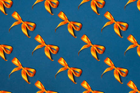 Trendy festive pattern. Orange bows on a blue background. Merry Christmas, St. Valentines Day, Happy Birthday and other holidays concept.の写真素材