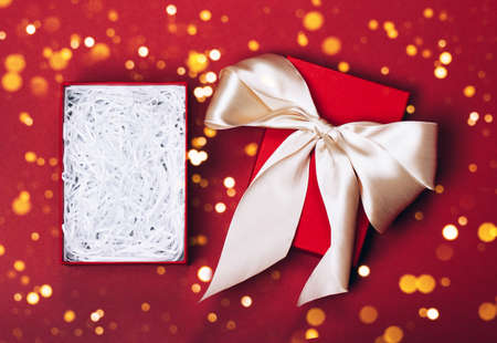 An opened gift box in which you can easily put any item. Red festive background and golden bow....