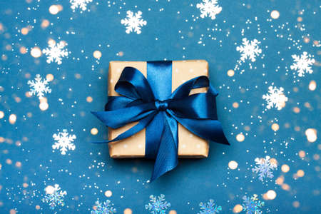 Attractive gift with blue ribbon on a blue background. Snow and lights. Merry Christmas, New Year, winter concept.の写真素材