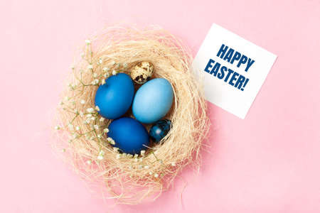 Easter eggs in blue colors in a nest on the pink background. Greeting card. Stylish decoration for Easter, zero waste concept. Flat lay.の写真素材